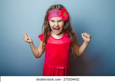 Girl European Appearance Haired Child Of Seven In Red Bright Dress On A Gray Background Shouts, Anger, Anger