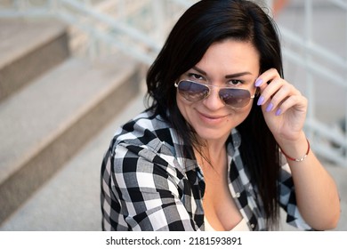 A girl of European appearance sits on the steps in the street with glasses. Close-up.