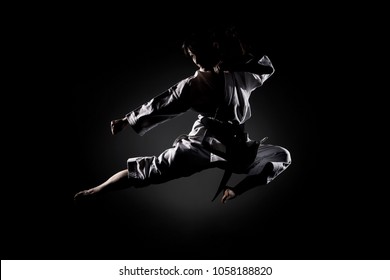 girl exercising karate, kick in the air against black background