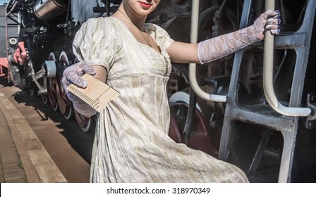 The Girl Expects Embarkation To A Train Cute Lady Woman Wear Retro Vintage Elegant White Dress Stand On Stairs And Hold In Hand Ticket For Conductor, Guide, Trainman Of Locomotive