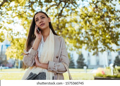 Girl With An Expression Of Anxiety And Empathy Speaks On The Phone Against A Background Of Yellow Leaves On Tree Branches