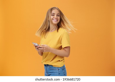 Girl Feeling Happy Receiving Message From Him. Portrait Of Carefree Charming Woman With New Haircut Waving Head Standing Half-turned, Turning To Camera With Pleased Cute Smile Holding Smartphone