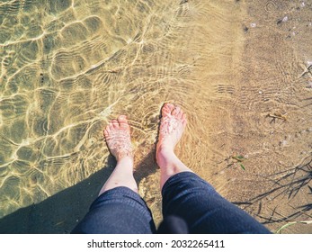 Girl feet in clear seawater on a sand beach