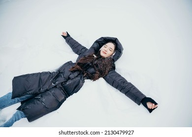 The Girl Fell Into The Snow And Makes A Snow Angel. An Adult Girl Behaves Like A Child And Wallows In The Snow.