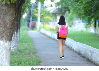 Girl Female Teenager With Black Hair In A Bob White East Asian Woman Green Park With A Backpack Background. Lady Walking, Goes, Walk Away, Look At The Camera.