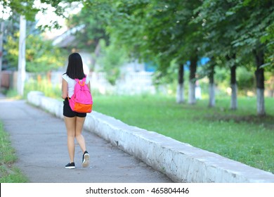 Girl Female Teenager With Black Hair In A Bob White East Asian Woman Green Park With A Backpack Background. Lady Walking, Goes, Walk Away, Look At The Camera.