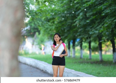 Girl Female Teenager With Black Hair In A Bob White East Asian Woman Green Park With A Backpack Background. Lady Walking, Goes, Walk Away, Look At The Camera.