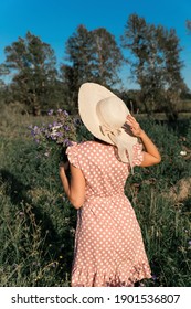 Girl In A Field With Flowers. Vintage Girl In A Calico Dress And Straw Hat With A Bouquet Of Wild Flowers