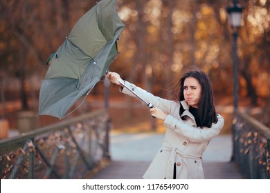 Girl Fighting The Wind Holding Umbrella Raining Weather. Autumn woman having problems in windy storm

