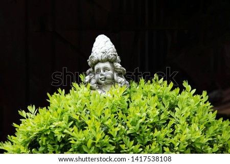 Girl figure made of stone behind a bush