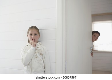 Girl with finger on lips standing by boy peeking round door