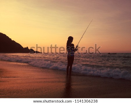 Girl fishing on the shore of the beach
at sunset