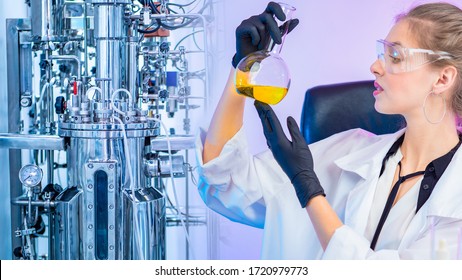 Girl With A Flask On The Background Of A Laboratory Bioreactor. Biochemistry. Research In The Field Of Pharmacology. The Reaction Of Fermentation. Laboratory Equipment.