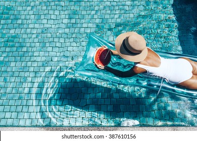 Girl floating on beach mattress and eating watermelon in the blue pool. Tropical fruit diet. Summer holiday idyllic. Top view.