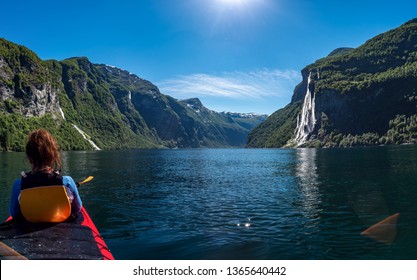 Girl Floating On A Kayak Over The Geiranger Fjord Overlooking The Waterfall Of Seven Sisters In Norway