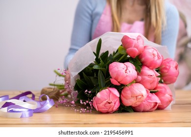 A Girl Florist Holds A Bouquet Of Pink Peonies Wrapped In White Craft Paper. Creation Of Beautiful Bouquets. Flower Studio