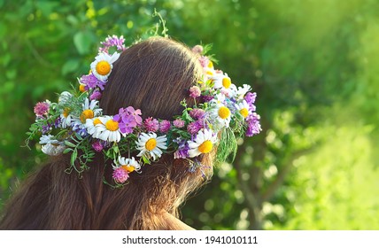girl in flower wreath on green sunny natural background, rear view. Floral crown, symbol of summer solstice. traditional Slavic ceremony on Midsummer, wiccan Litha sabbat. pagan holiday Ivan Kupala