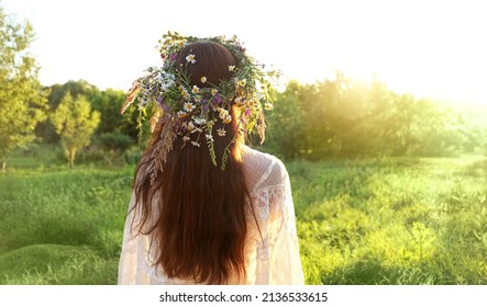 girl in flower wreath on meadow, sunny green natural background. Floral crown, symbol of summer solstice. Slavic ceremony on Midsummer, wiccan Litha sabbat. pagan holiday Ivan Kupala