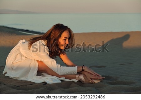 A girl in a fly white dress dances and poses in the sand desert at sunset.