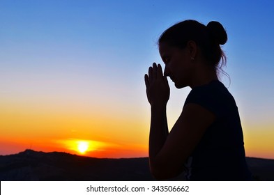 Girl folded her hands in prayer. Beautiful sunset. Colorful sky. Tenderness and serenity