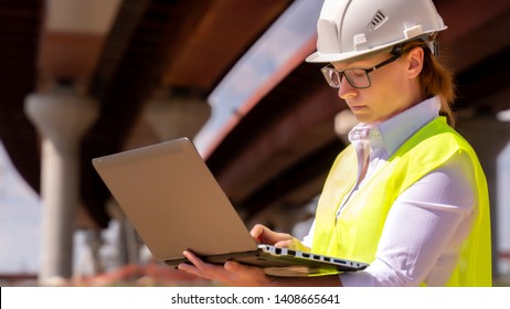 Girl foreman with laptop at construction site. female engineer works on computer under overpass under construction.
