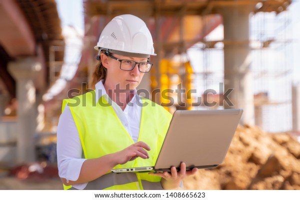 Girl foreman\
with laptop at construction site. female engineer works on computer\
under overpass under\
construction.