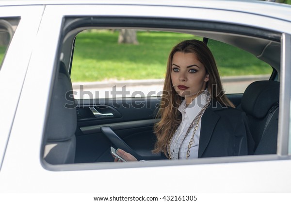 Girl in formal clothes reads the information from\
the tablet while sitting on the back seat of the car. Concept:\
transport, lifestyle,\
fashion