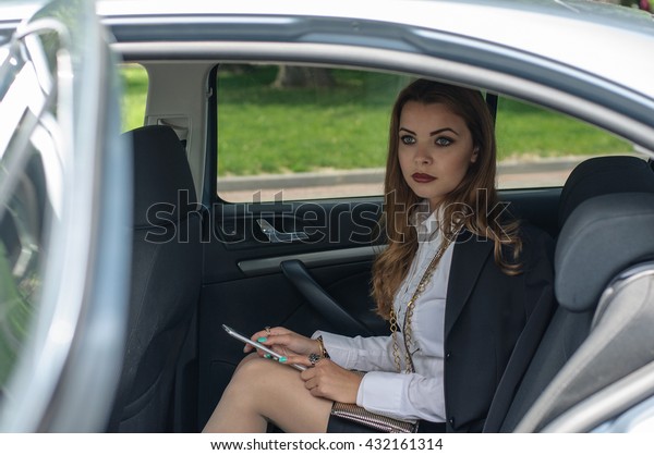 Girl in formal clothes reads the information from\
the tablet while sitting on the back seat of the car. Concept:\
transport, lifestyle,\
fashion