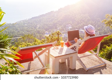 Girl Freelancer Work Typing On Laptop And Looking At Monitor With Beautiful View And Cocktail Outdoors Sun Sky And Greens. Traveling With A Computer. Online Dream Job On The Island In Thailand Concept