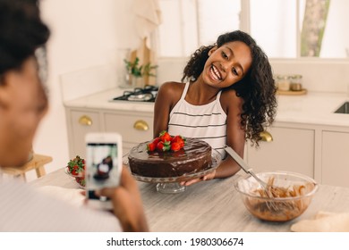 Girl with freshly baked cake being photographed by mother in kitchen. Mother taking picture woman daughter making cake. - Powered by Shutterstock