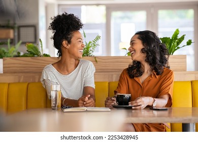 Girl friends laughing and enjoying coffee. Multiethnic woman friends in a conversation during break between one university lesson and another. Black girl talking with her friend at coffee shop.