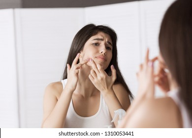 Girl frowning looking pimple on her cheek in mirror.