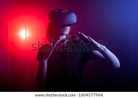 girl gamer in modern virtual reality glasses plays boxing on a dark red-blue background, a woman begins a virtual hand-to-hand fight