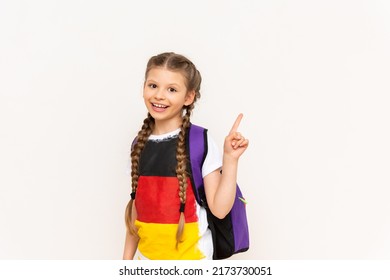 A girl with a German flag on a T-shirt. A child with pigtails swings a book and smiles on a white isolated background. Language courses for children.