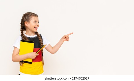 A girl with a German flag on a T-shirt points at your advertisement with her index finger on a white isolated background. Copy space. German language courses for children.
