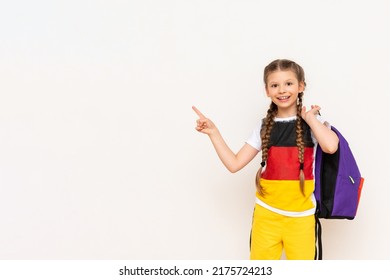 A girl with a German flag on a T-shirt. A child with pigtails swings a book and smiles on a white isolated background. Language courses for children.