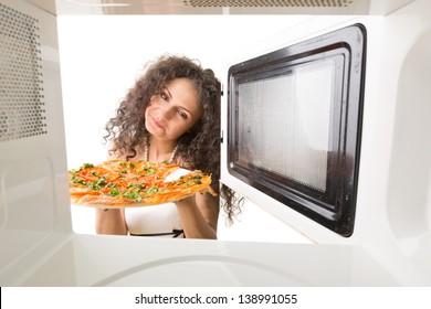 The girl gets a pizza out of the microwave