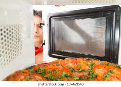 The girl gets a pizza out of the microwave