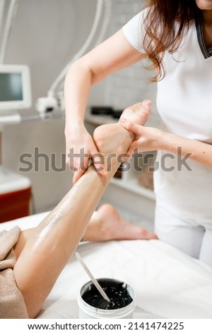 The girl is given an anti-cellulite foot massage with a black scrub cream. Depilation of legs in a beauty salon. Close-up of the massage. Depilation close-up.