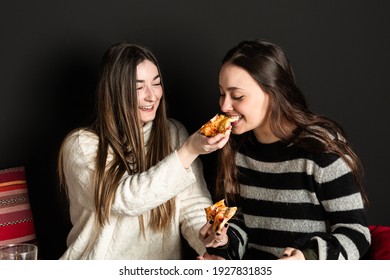 A Girl Gives A Piece Of Pizza To Another Girl To Eat, And She Bites Into It.