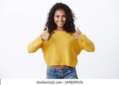 Girl giving her approval like idea. Happy attractive african american young woman in yellow autumn sweater showing thumbs-up gesture and smiling, nod approvingly, accept good plan, white background - Shutterstock ID 1498299476
