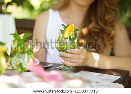 A girl with a glass sits in a cafe. A glass of lemonade in the hands of a girl.