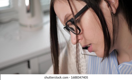 Girl With Glasses Holds An Uncomfortable Phone And Talks To Someone Intently, Typing Something With Both Hands Into Laptop Or Writing To Notebook. Freelancer Girl At Work Business Conversation Concept