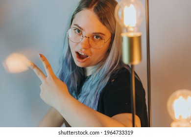 Girl With Glasses Next To Light Bulbs Shows Two Fingers