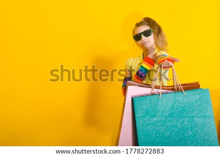 A girl with glasses stands with packages and poses on an orange background.