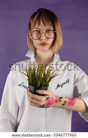 Girl in glasses whit bodyart on a lilac background, flower in hands
