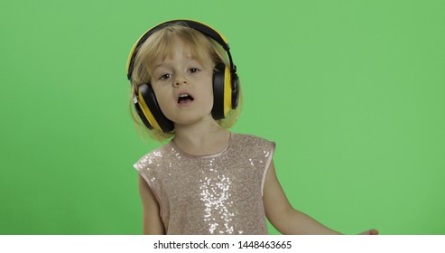 Girl In Glossy Dress And Headphone Listening To Music And Singing. Happy Four Years Old Girl. Pretty Little Child, 3-4 Year Old Blonde Girl. Make Faces And Smile. Green Screen. Chroma Key