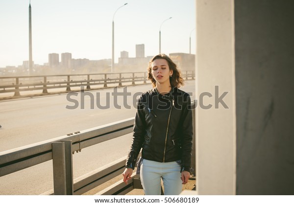 girl goes on road bridge. lonely young woman\
in black Leather jacket autumn, walking over the bridge which goes\
transport.