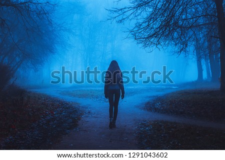 Girl goes on the road in a mysterious forest. Background for wallpaper. Strange forest in a fog with red leaves. Mystic atmosphere. Dark scary park. Paranormal another world.