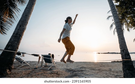 Girl goes on slackline at sunset on a tropical beach. Young woman practices on slackline by the ocean on a tropical island in the evening - Powered by Shutterstock